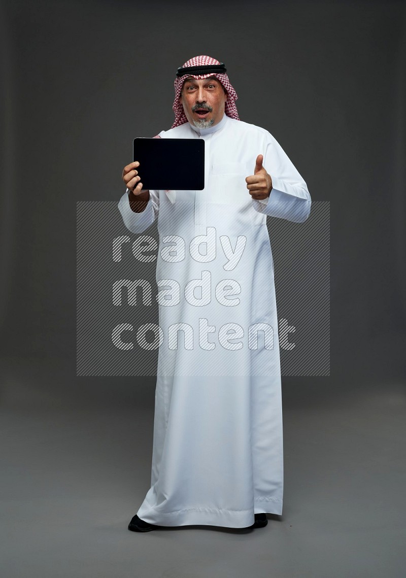 Saudi man with shomag Standing working on tablet on gray background