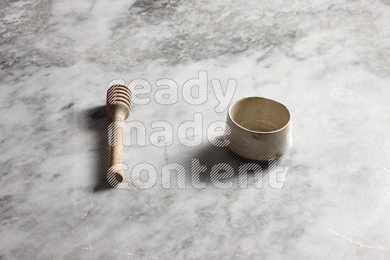 Beige Pottery Bowl with wooden honey handle on the side with grey marble flooring, 45 degree angle
