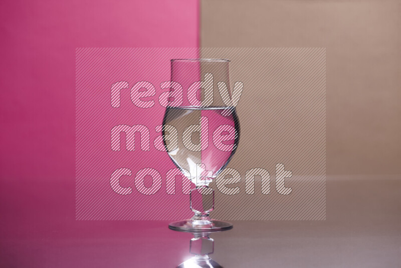 The image features a clear glassware filled with water, set against pink and beige background