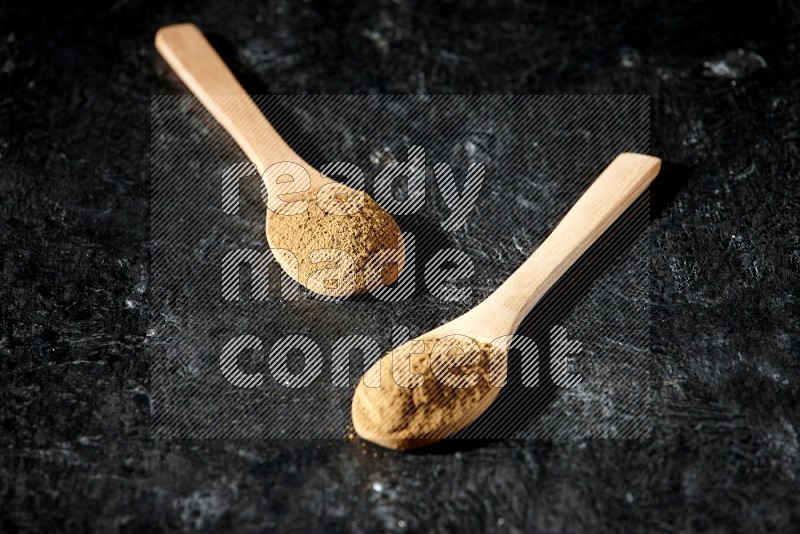 Wooden spoons full of allspice powder on a textured black flooring
