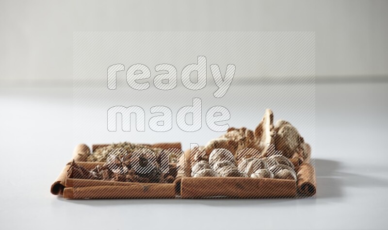 4 مربعات من أعواد القرفة ممتلئة باليانسون والزنجبيل والكمون وجوزة الطيب على أرضية بيضاء