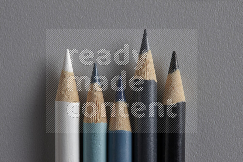 A collection of colored pencils arranged showcasing a gradient of white, grey and black hues on grey background
