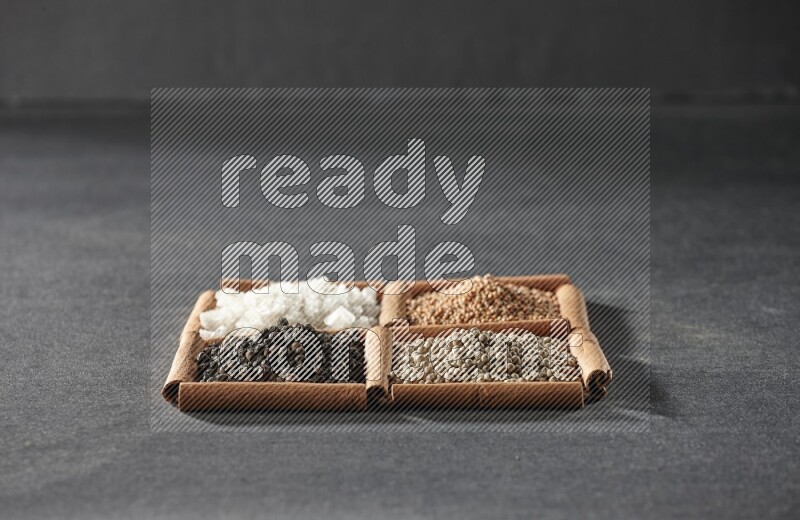 4 مربعات من عيدان القرفة ممتلئة بحبوب الفلفل الأسود والفلفل الأبيض والملح الأبيض وحبوب الخردل على أرضية سوداء