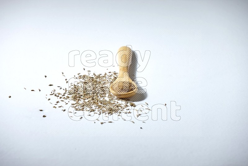 A wooden spoon full of cumin powder and cumin seeds beside it on white flooring