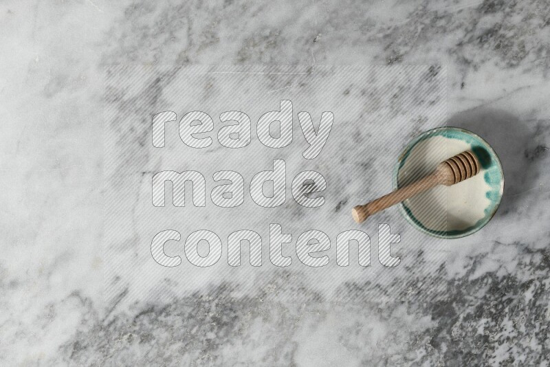 Multicolored pottery bowl with wooden honey dipper in it on grey marble background