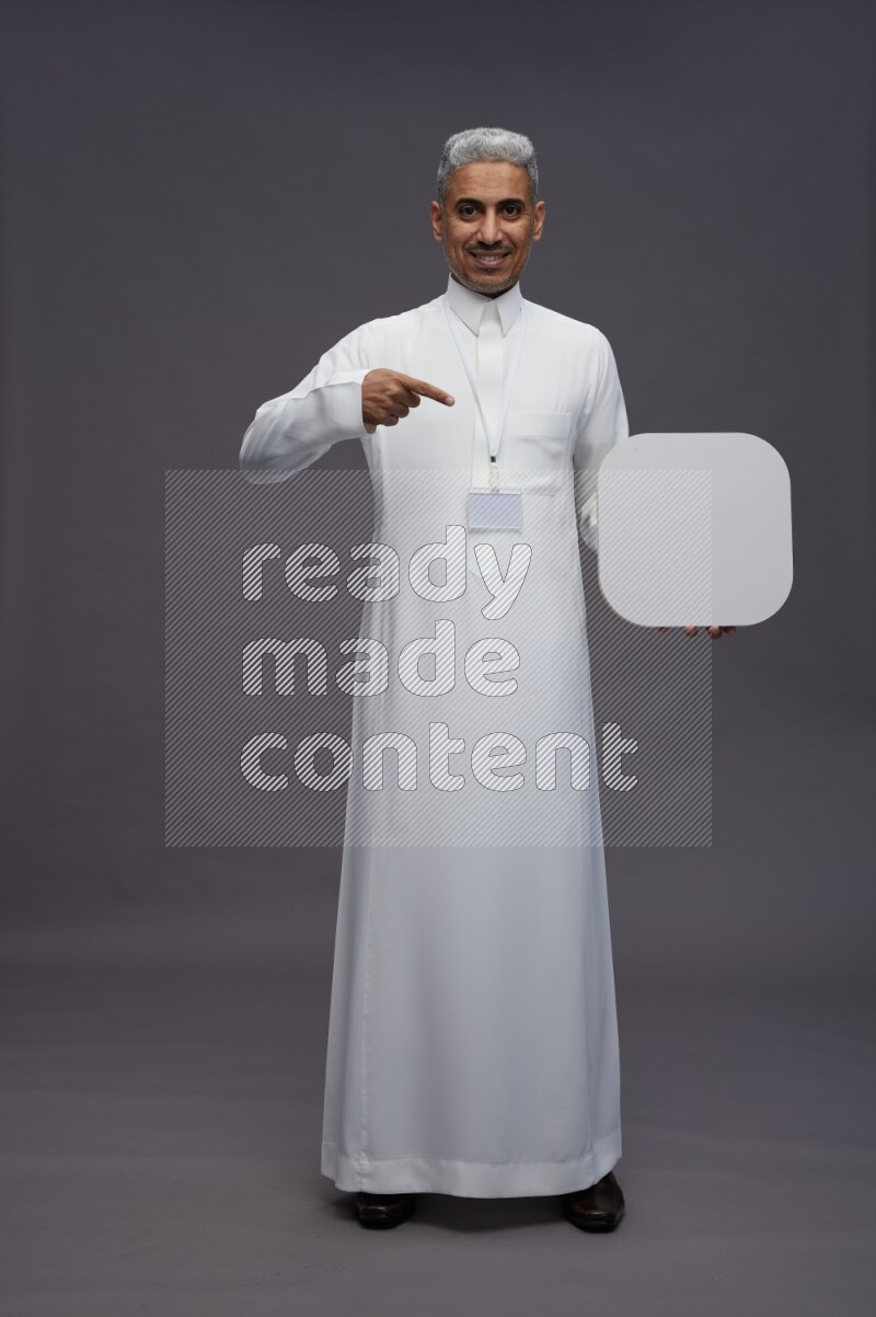 Saudi man wearing thob with neck strap employee badge standing holding social media sign on gray background