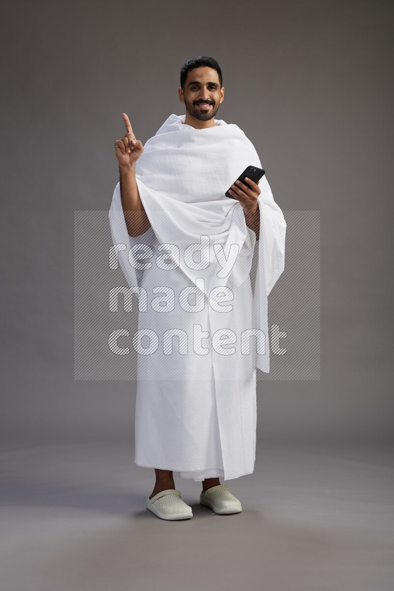 A man wearing Ehram Standing texting on phone on gray background