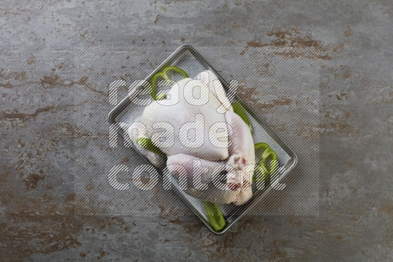 whole Raw chicken on a small oven trey direct on a rustic grey background
