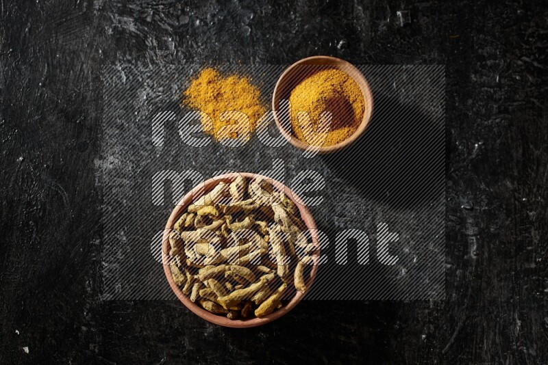 وعاءان خشبيان، أحدهما ممتلئ ببودرة الكركم والآخر بأصابع الكركم المجففة، على خلفية سوداء