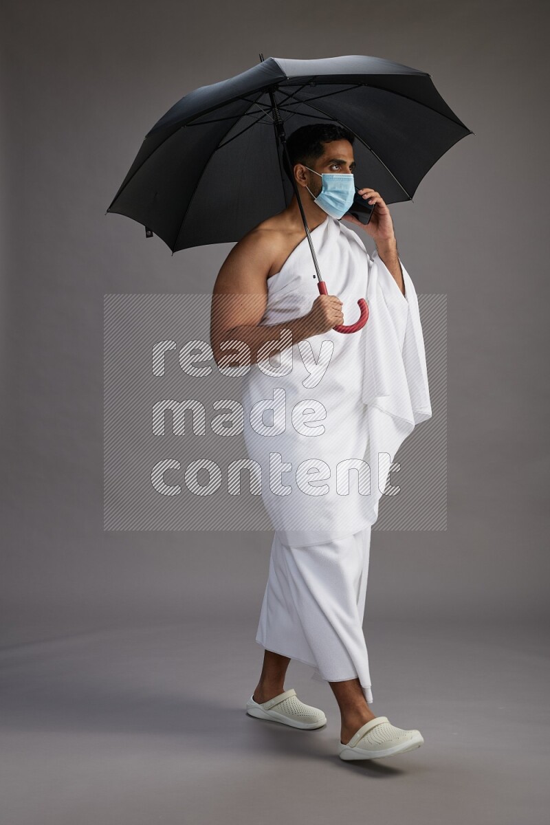 A man wearing Ehram and mask Standing holding umbrella on gray background on gray background