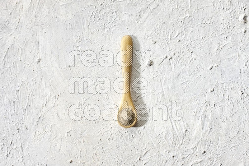 A wooden spoon full of white pepper powder on textured white flooring