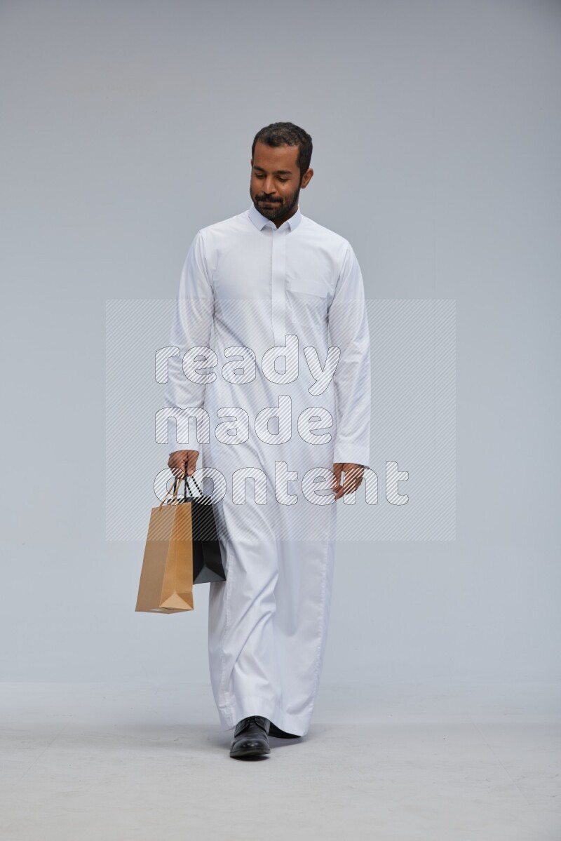 Saudi man Wearing thob standing holding shopping bag on Gray background