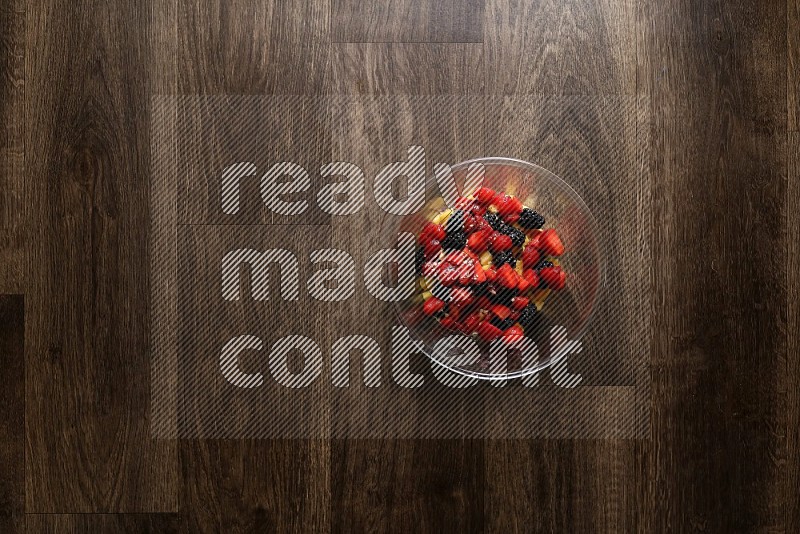 A glass bowl full of tuna, avocado, mango, blackberry and strawberry on wooden background