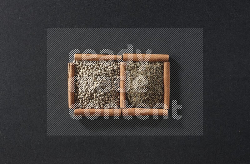 مربعان من أعواد القرفة ممتلئان بحبوب الفلفل الأبيض وحبوب الكمون علي خلفية سوداء