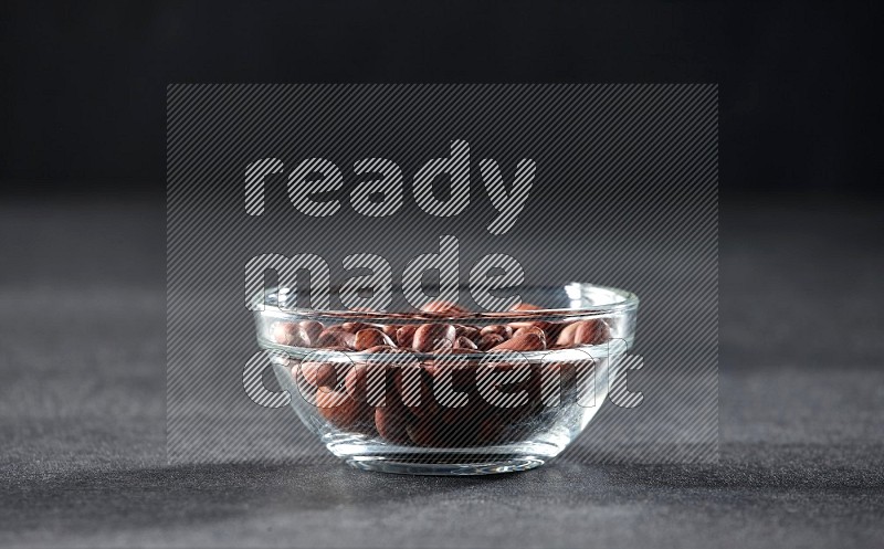 A glass bowl full of red skin peanuts on a black background in different angles