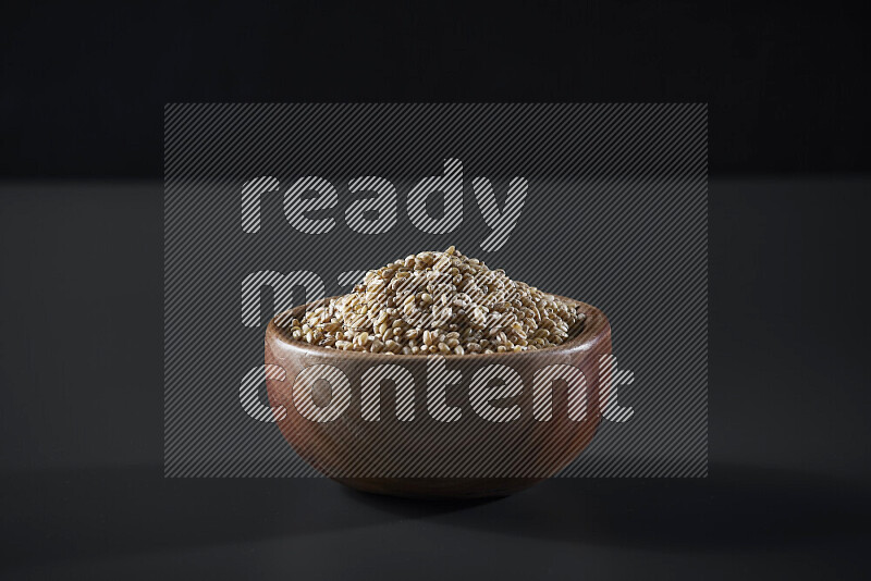 Hulled wheat in a wooden bowl on grey background