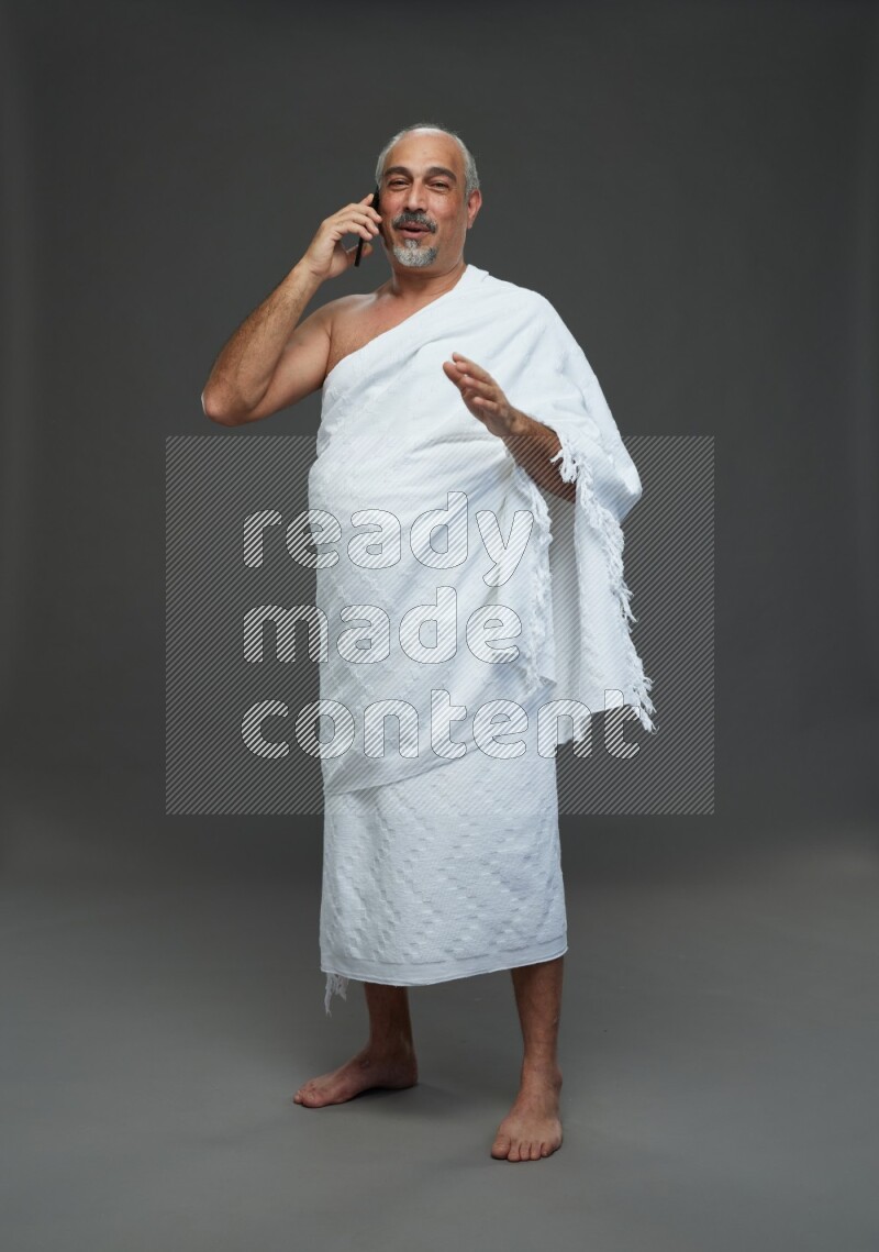 A man wearing Ehram Standing talking on phone on gray background