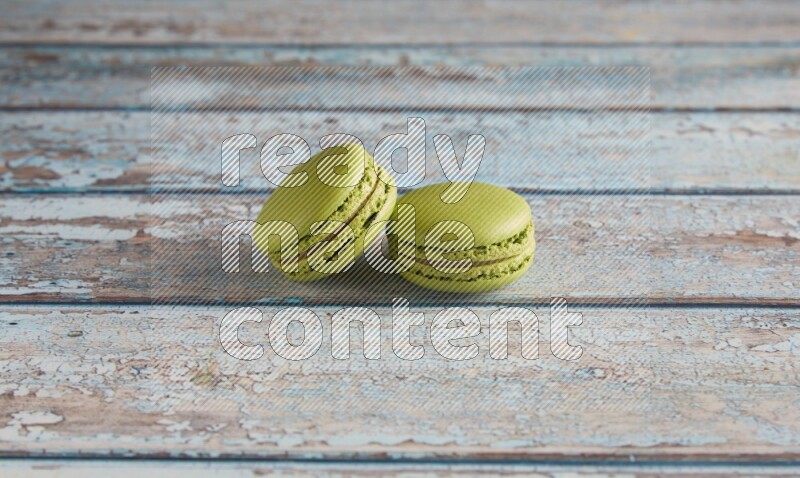 45º Shot of two Green Pistachio macarons on light blue wooden background