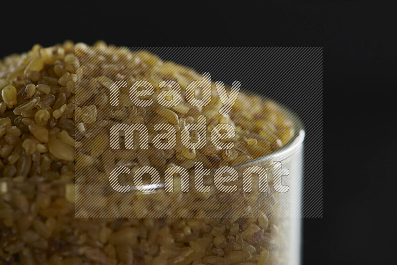 Coarse bulgur in a glass jar on black background