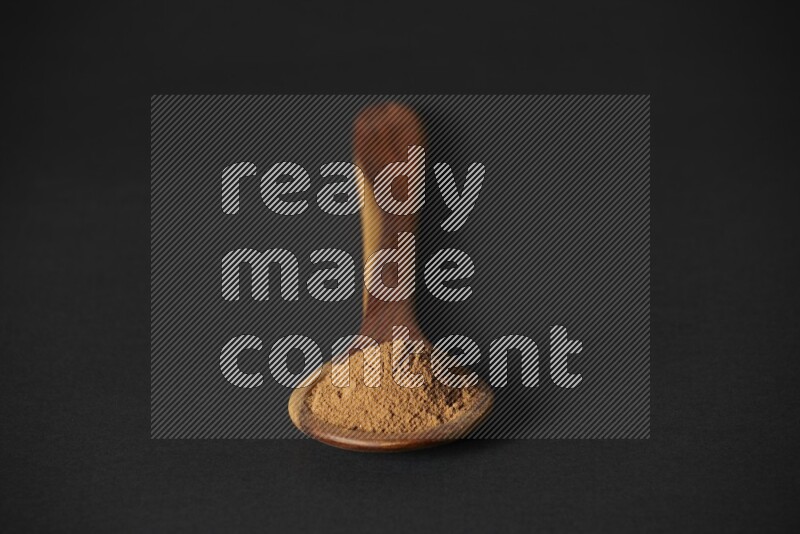 Cinnamon powder in a spoon ladle on black background