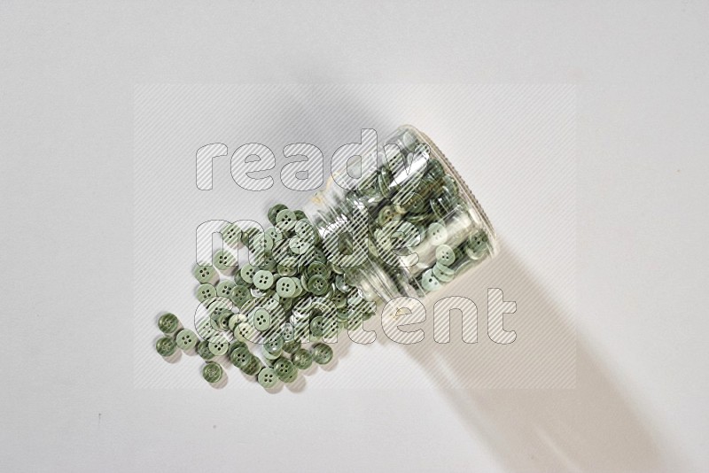 A glass jar full of colored buttons on grey background