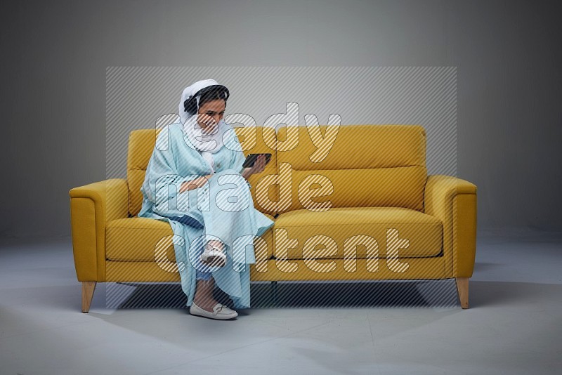 A Saudi woman sitting on a yellow Sofa Watching a Movie wearing Blue Abaya