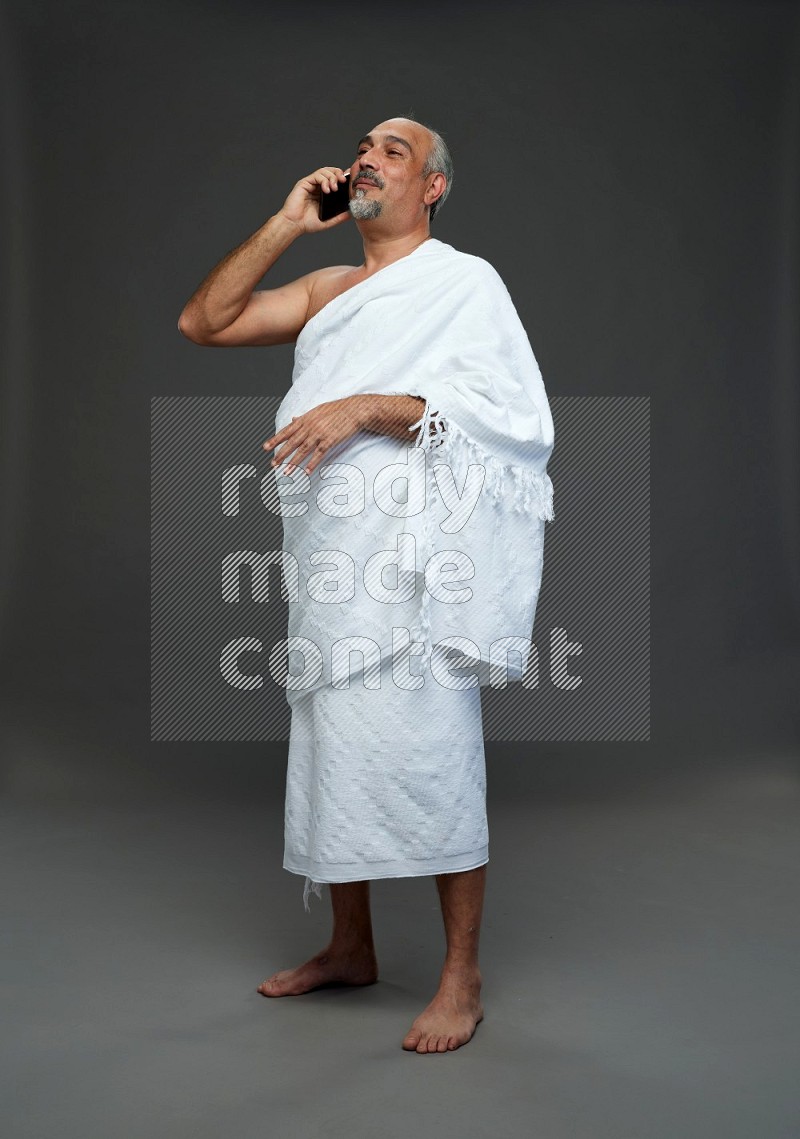 A man wearing Ehram Standing talking on phone on gray background