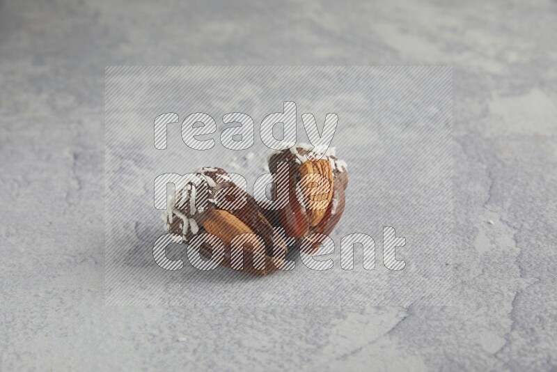 Two Almond stuffed dates covered with dark chocolate and coconut on a light grey background