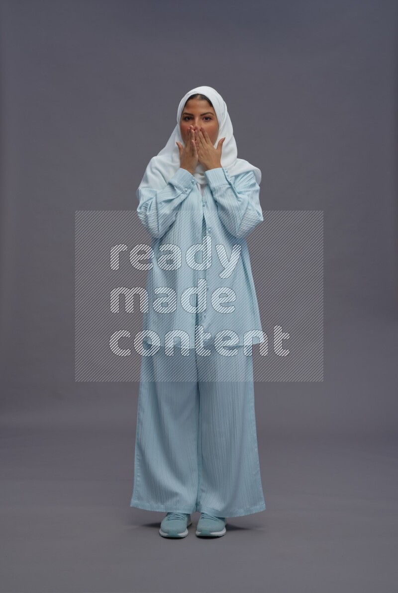 Saudi woman wearing hijab clothes standing interacting with the camera on gray background