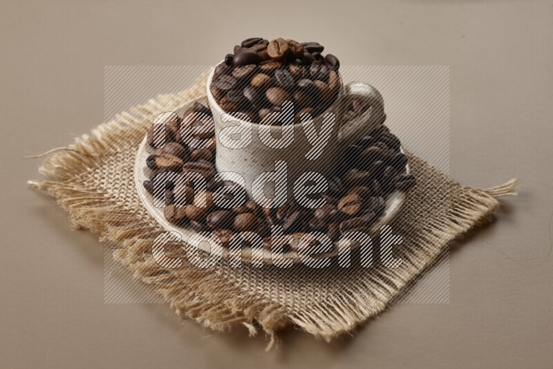 A beige pottery cup full of roasted coffee beans on beige background