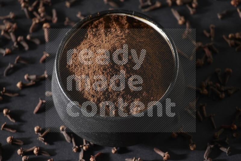 وعاء فخاري أسود ممتلئ ببودرة القرنفل وحبوب القرنفل على خلفية سوداء