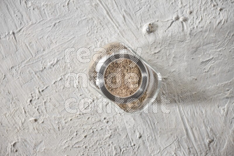 فلفل أسود مطحون في وعاء زجاجي علي خلفية بيضاء