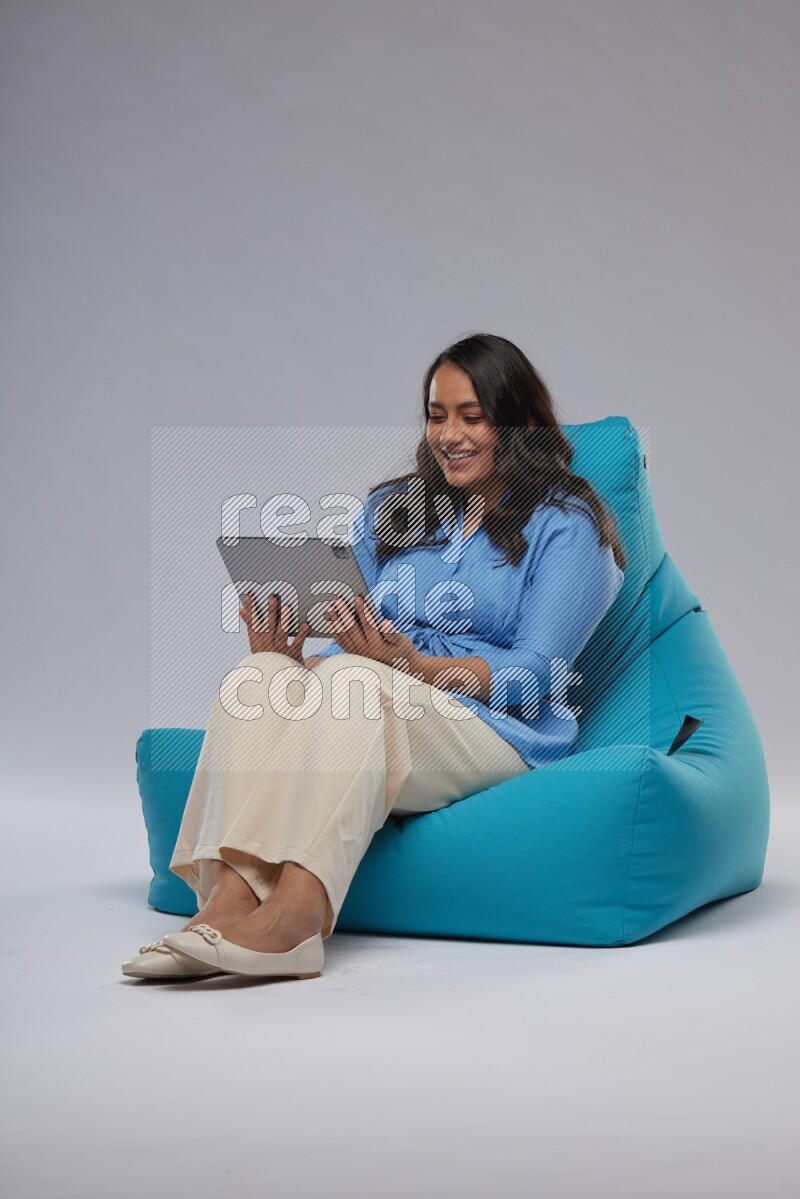 A woman sitting on a blue beanbag and working on tablet