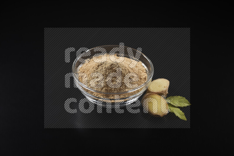 A glass bowl full of ground ginger powder on black background