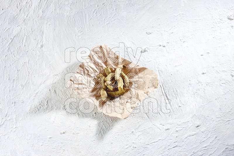 Dried turmeric whole fingers in a crumpled piece of paper on textured white flooring