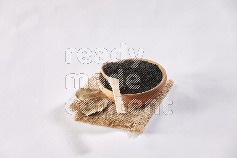 A wooden bowl and wooden spoon full of black seeds on a piece of burlap on a white flooring in different angles