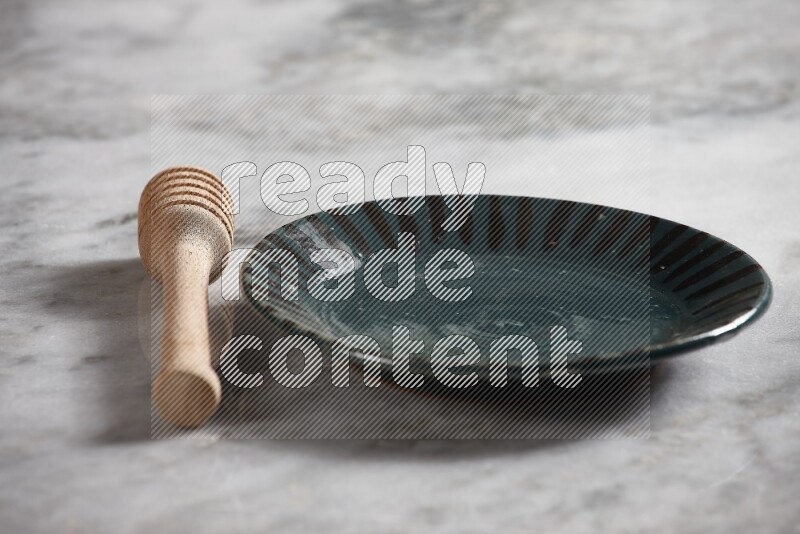 Multicolored pottery plate with wooden honey dipper on the side on grey marble background