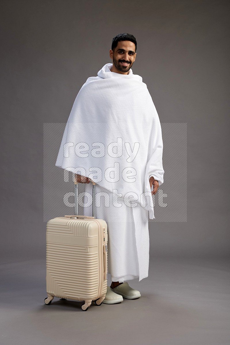 A man wearing Ehram Standing holding traveling bag on gray background