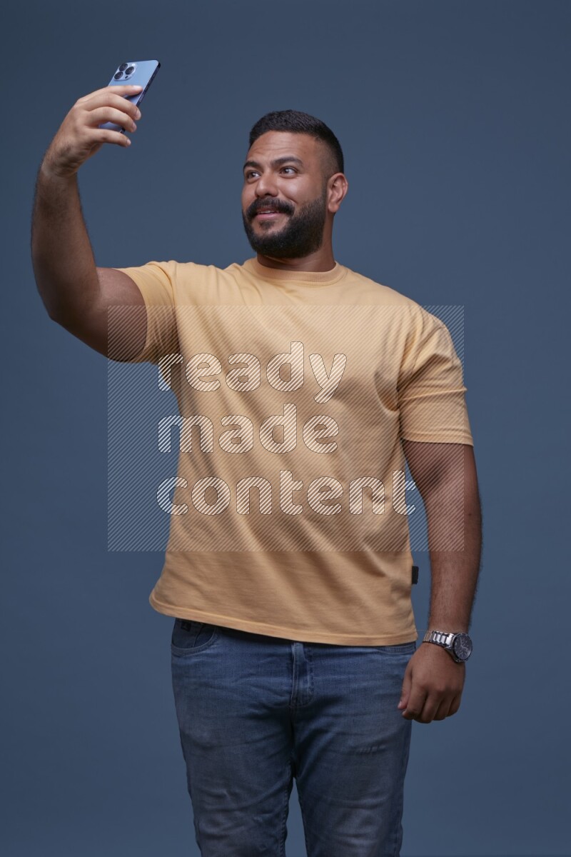 رجل يرتدي بنطال ازرق جينز وقميص اصفر بأكمام قصيره يصور نفسه بجواله