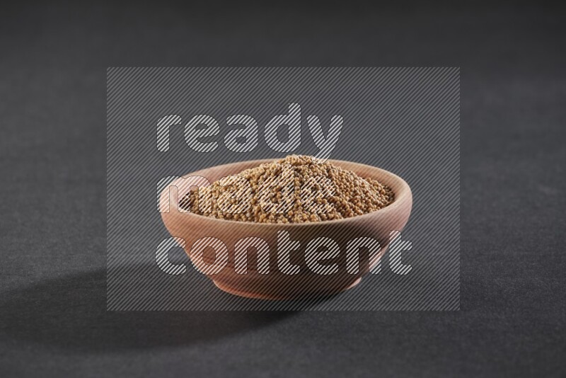 A wooden bowl full of mustard seeds on a black flooring