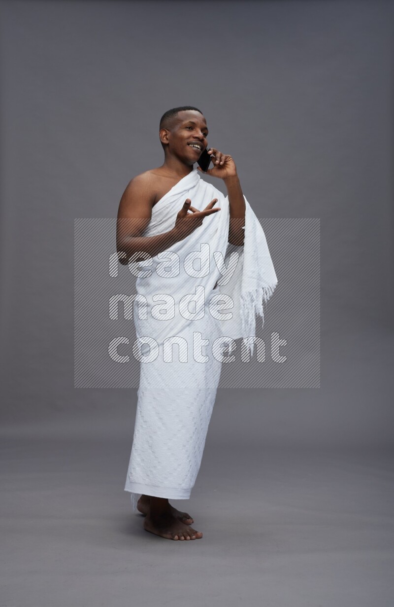 A man wearing Ehram Standing talking on phone on gray background