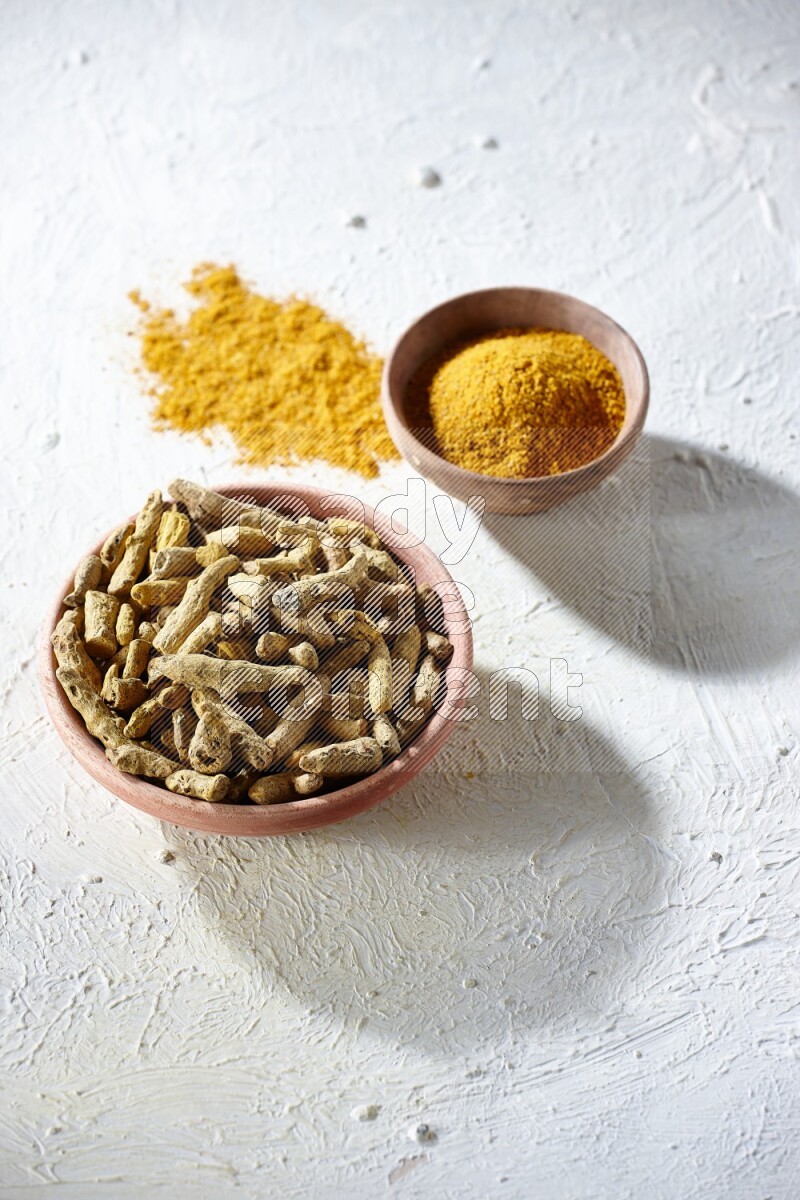 وعاءان خشبيان، أحدهما ممتلئ ببودرة الكركم والآخر بأصابع الكركم المجففة، على خلفية بيضاء