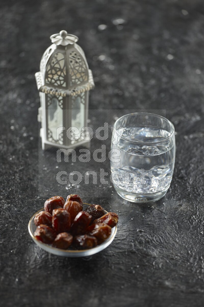 A white lantern with different drinks, dates, nuts, prayer beads and quran on textured black background