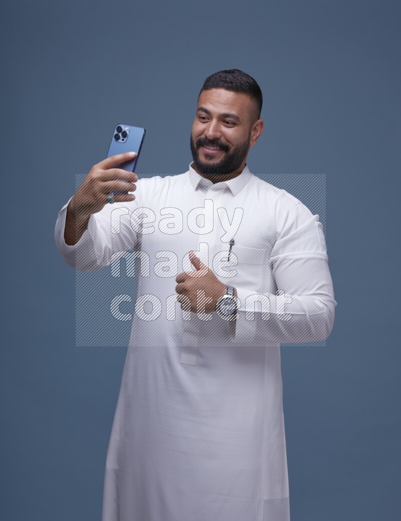 A Saudi man Taking A Selfie on Blue Background wearing Saudi Thob