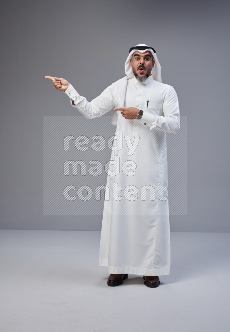 Saudi man Wearing Thob and white Shomag standing interacting with the camera on Gray background