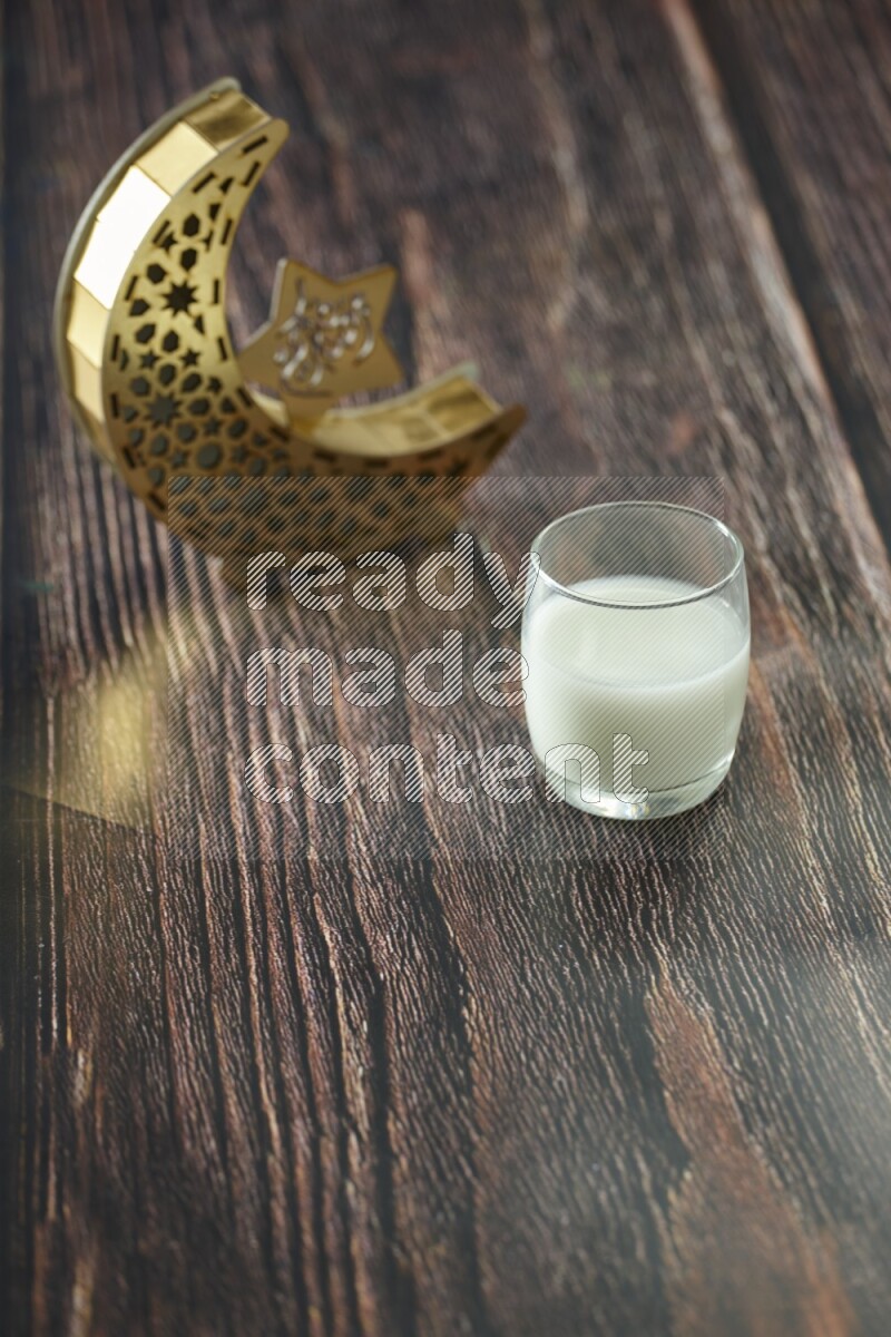 فانوس خشبي هلالي باللون الذهبي مع مشروبات مختلفة وتمر ومكسرات وسبحة صلاة وقرآن على خلفية خشبية بنية