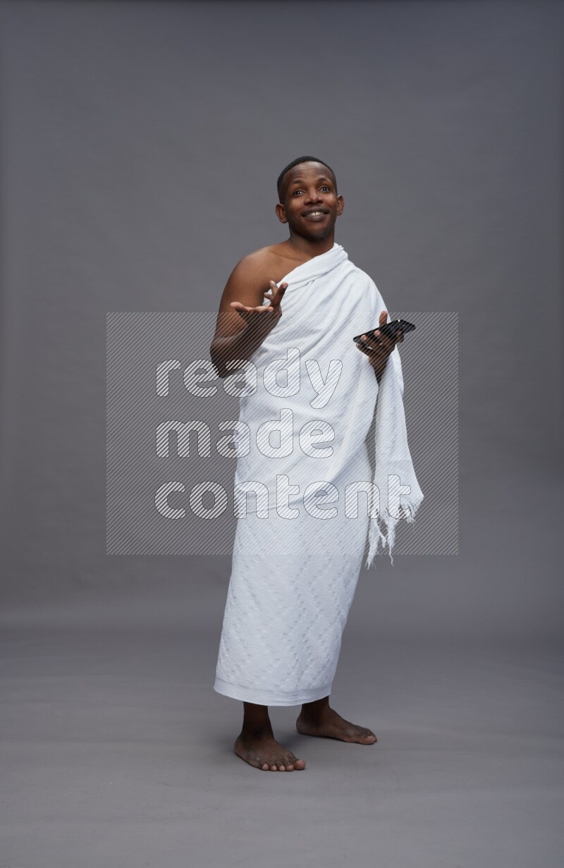 A man wearing Ehram Standing texting on phone on gray background