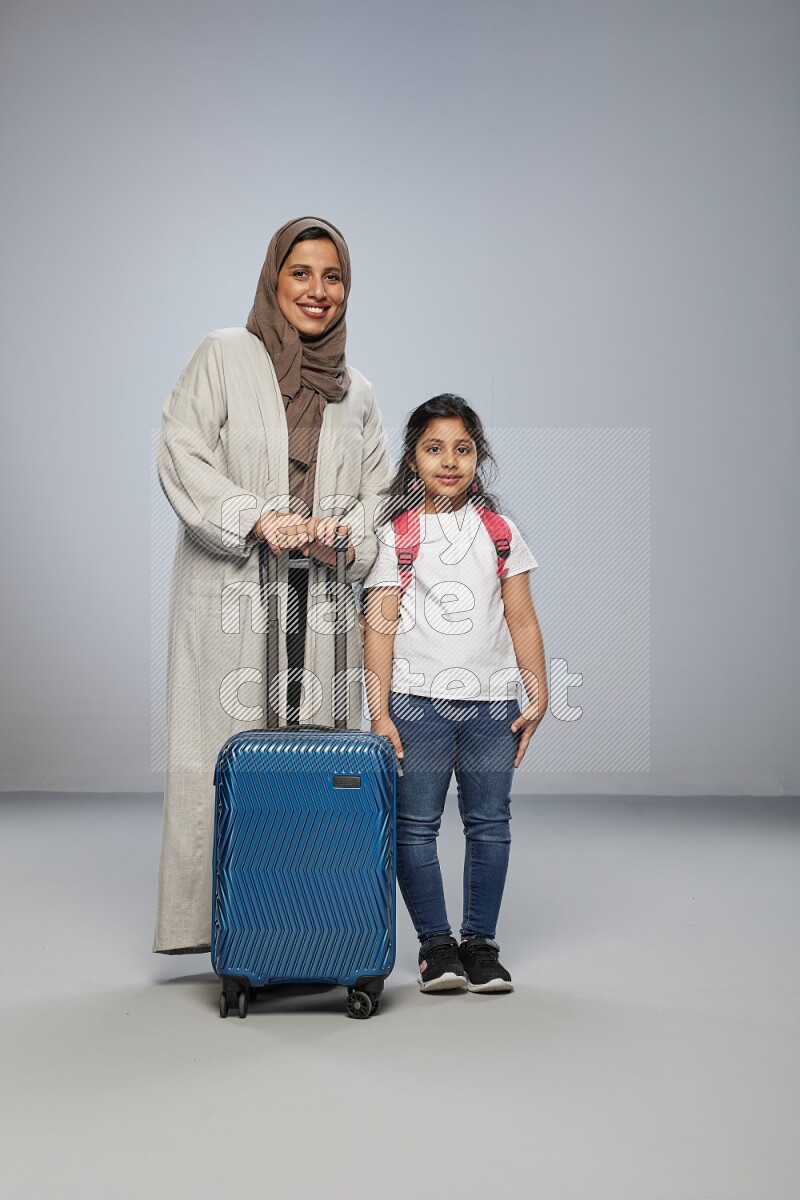 Mom and daughter standing pulling a carry-on bag on gray background