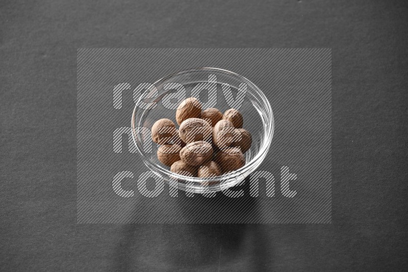 A glass bowl full of nutmeg on black flooring