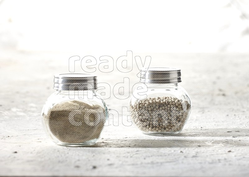 2 Herbal Glass jar full of white pepper beads and powder on textured white flooring